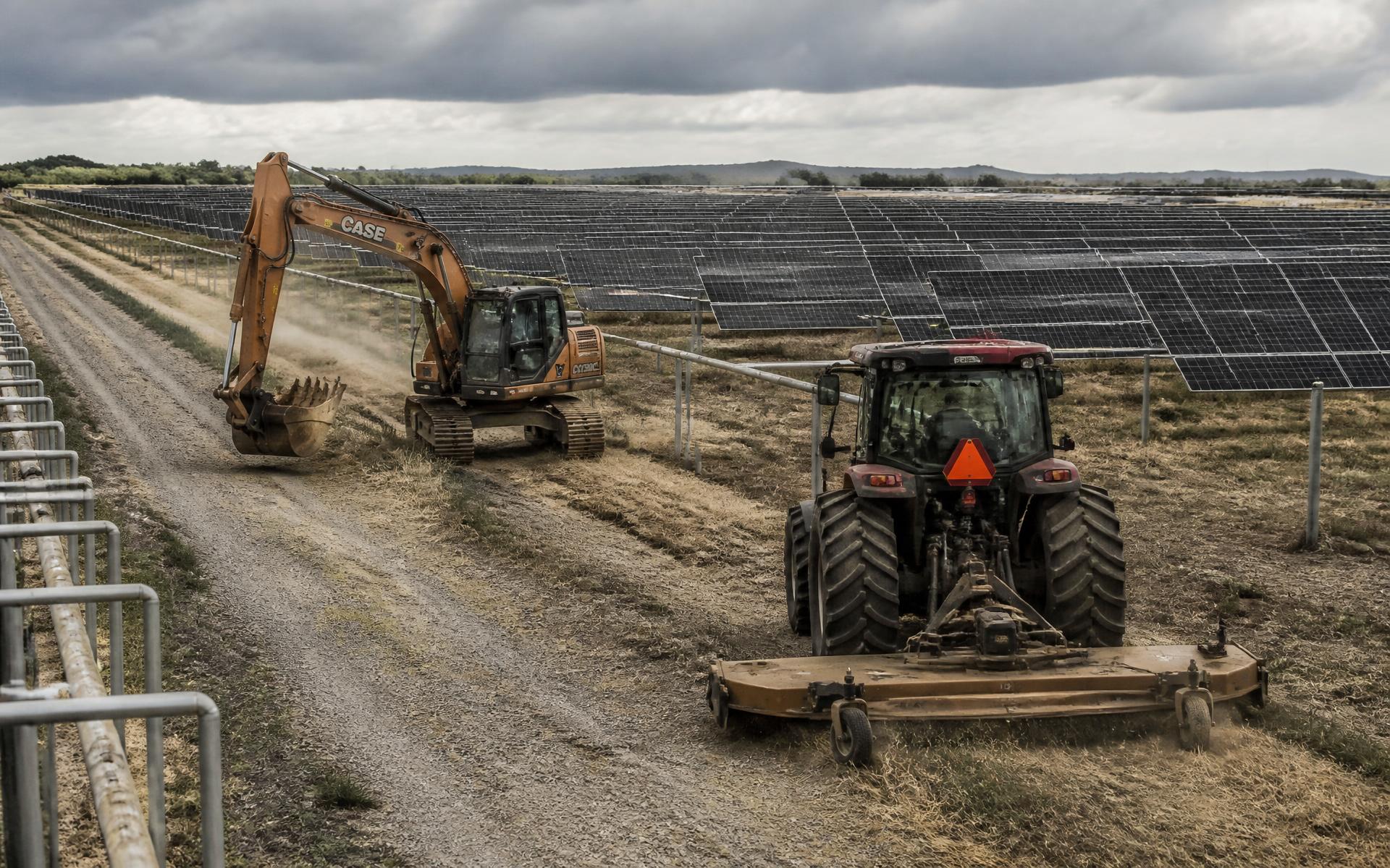 Heavy equipment mowing and grading between rows of a utility-scale solar field